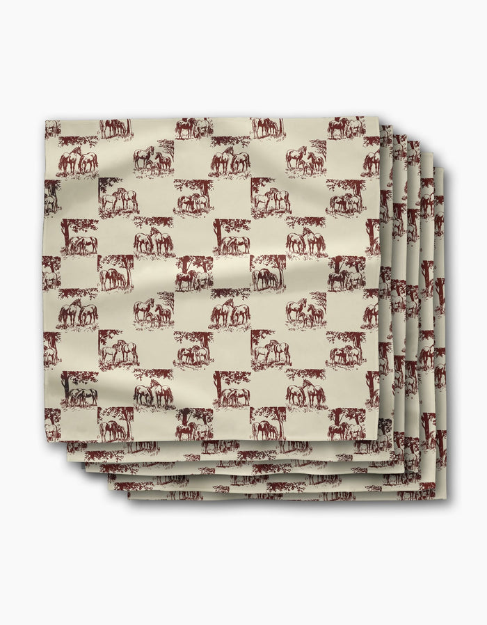 Four folded Geometry Horse Check Cream dinner napkins, featuring a repeating brown horse pattern on beige, are stacked neatly on a white background. These reusable napkins bring charm and sustainability to your table setting.