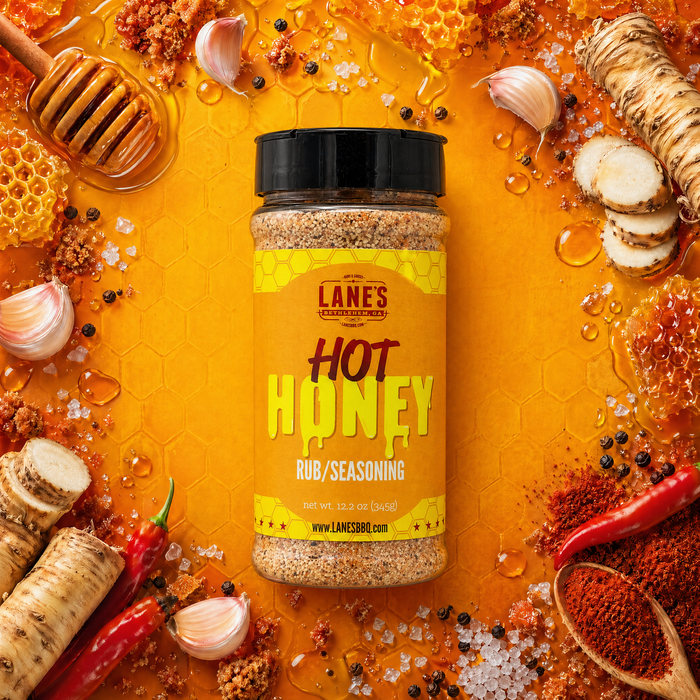 Bottle of Lanes Hot Honey Rub/Seasoning surrounded by honeycomb, garlic, and spices on a bright yellow background.