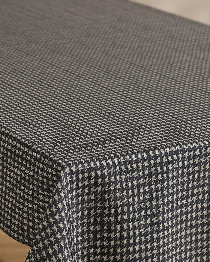 A close-up of a table covered with Geometry’s Houndstooth Black tablecloth, featuring its lightweight fabric and crisp black and white houndstooth pattern draping smoothly over the softly rounded edge.