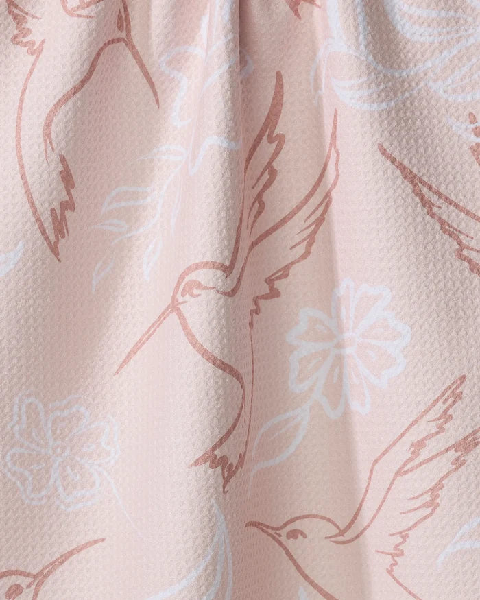 Close-up of Elena Fay’s Hummingbirds tea towel in light pink, featuring a subtle fabric texture and a white and light brown illustrated pattern of hummingbirds and flowers.