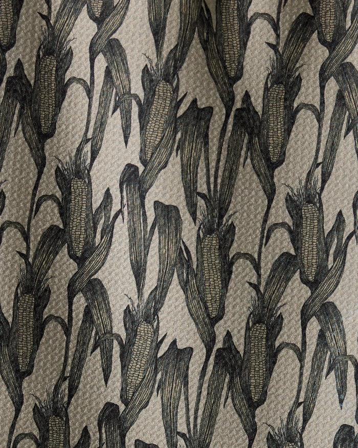Close-up of Husk, a bar towel by Geometry, featuring a repeating pattern of black corn cobs and leaves on a beige background. The illustration-style design highlights intricate details. Made from recycled materials.