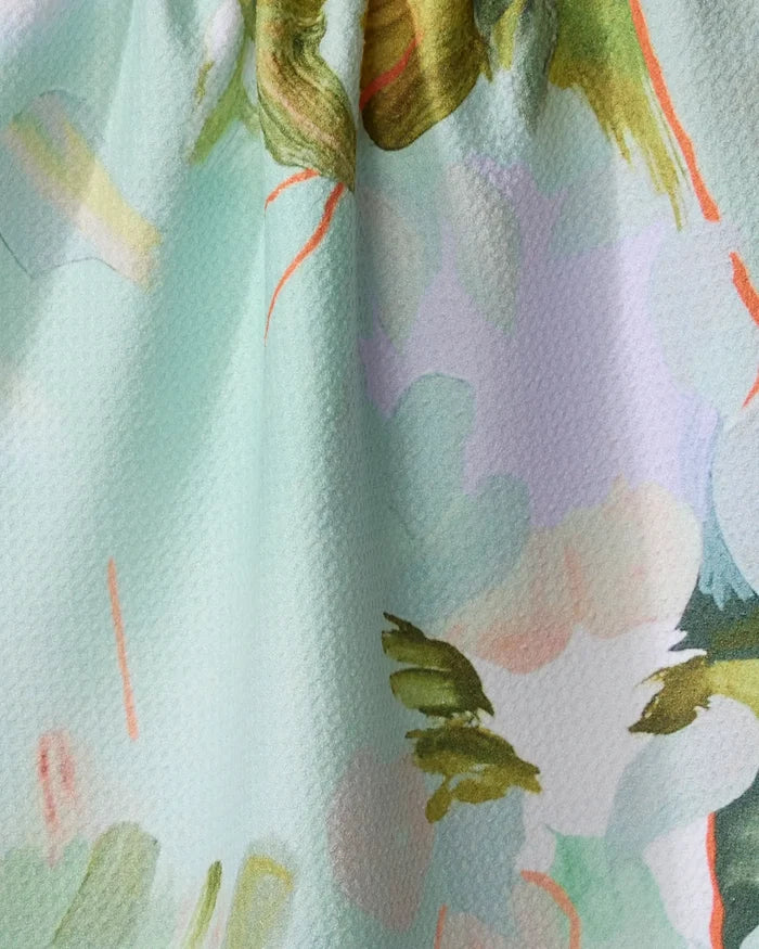 Close-up of Kristina Baker’s "If I Were An Orchard" recycled kitchen towel, featuring an abstract watercolor floral pattern in green, peach, and orange on light aqua. The softly gathered fabric creates gentle folds and textured shadows.