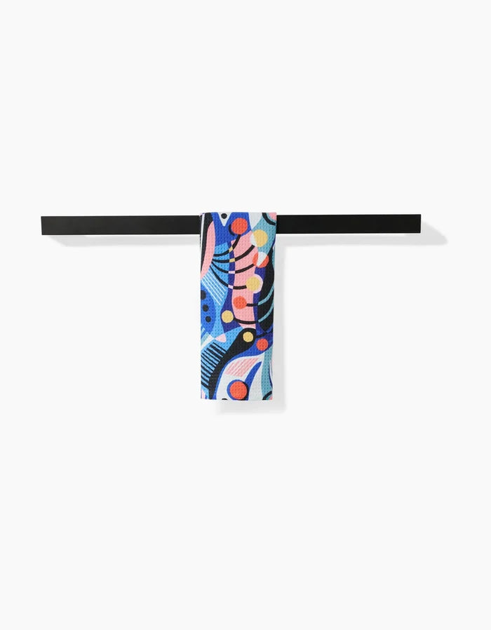A black horizontal bar displays the ultra-absorbent Imagined Realm Bar Towel by Masha Volnova, crafted from Geoweave fabric and adorned with blue, pink, orange, black, and white abstract shapes on a white background.