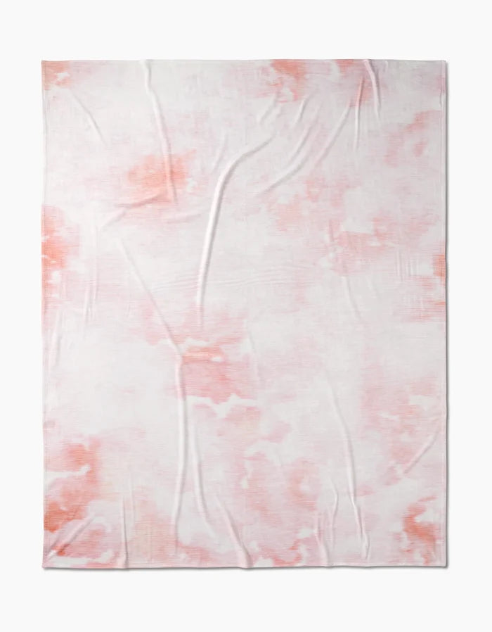 The Geometry In the Clouds Butter Blanket is a soft, rectangular throw with a subtle pink and white tie-dye pattern, designed for silky softness and gentle comfort.