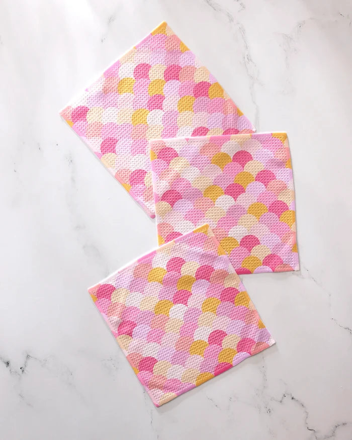 The GEOMETRY Inherit dishcloth set includes three super-absorbent towels in pink, yellow, and white scallop patterns, artfully displayed on a white marble surface.