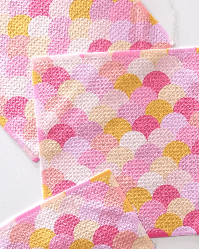 The GEOMETRY Inherit set features three eco-friendly dishcloths with a pink, yellow, and white scallop pattern, crafted from recycled materials and stylishly layered against a white background.