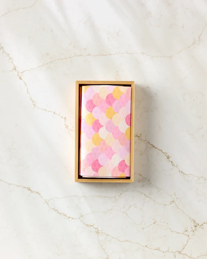 A rectangular box of GEOMETRY's Inherit eco-friendly kitchen towels, featuring a pastel scallop design with pink, yellow, and light purple arcs, rests on a light marble surface with soft shadows.