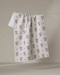 The Cole Strem "Inked Bloom" dish towel, featuring a black floral and dot pattern on white, is shown hanging over a clothesline against a neutral background.