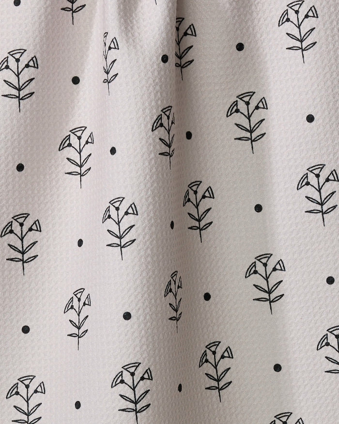 Close-up of Cole Strem's Inked Bloom dish towel, showcasing white textured fabric with a regular grid of simple black floral patterns and small dots.