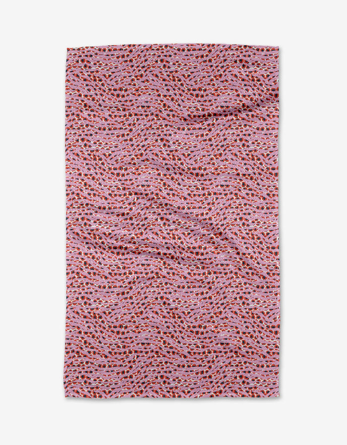 The Into the Wild tea towel by Happy Hemera features a wavy red, orange, and black pattern on pink. Made from recycled materials, this ultra-absorbent rectangular towel is shown laid flat with slight wrinkles.
