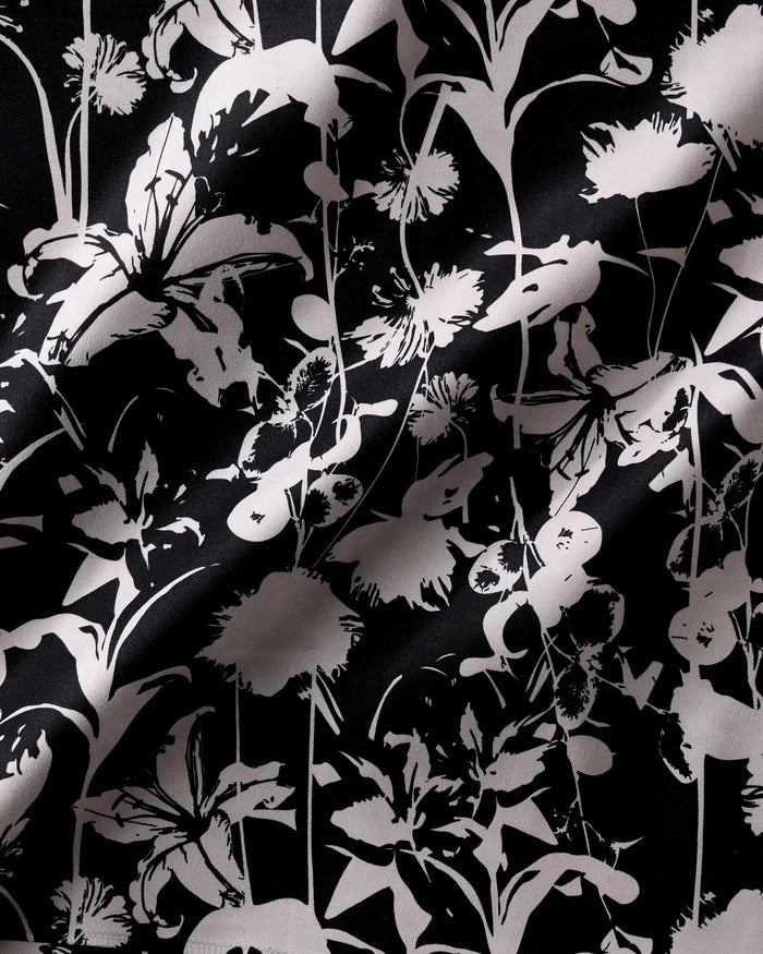 The Geometry Inverted Floral Black napkin set features black fabric with a white floral print in a random pattern of flowers and stems. Visible folds and gentle shadows add texture and depth to the reusable set.