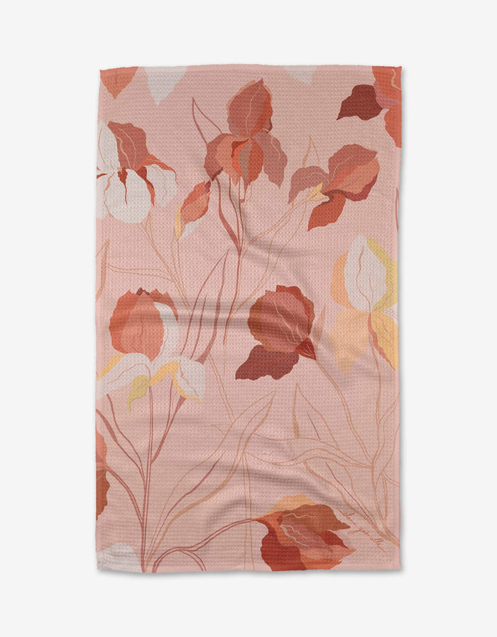 The Iris towel by Elana Gabrielle is rectangular and light pink, featuring a vibrant floral pattern. Made from ultra-absorbent Geoweave fabric, it has a subtly textured, slightly wrinkled surface.