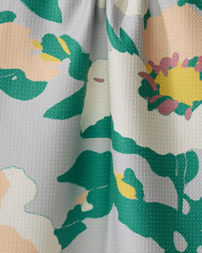 A close-up of Isla by Geometry: textured fabric with a colorful floral pattern—large green leaves and pink, yellow, cream flowers on light gray—perfect for a quick-drying tea towel made from recycled materials.
