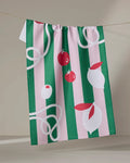 The Italian Mood tea towel by Marina Solodka hangs on a line, ultra-absorbent with green and pink stripes. It features charming illustrations of tomatoes, garlic bulbs, and white squiggly noodle-like lines.