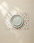 A plain light gray plate sits on the Geometry Italian Summer Grid Placemat, featuring a blue grid and small red and yellow floral pattern, atop a neutral tablecloth.