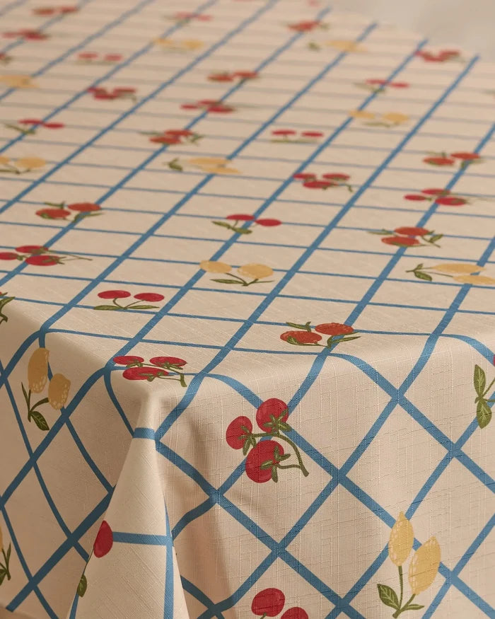The Geometry Italian Summer Grid tablecloth, in beige with a blue grid and red cherries with yellow lemons print, offers a lightweight, stain-resistant cover for your rectangular table.