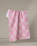 The Jaskin dish towel by Amy MacCready, with a pink geometric fan design on white, hangs on a clothesline against a light gray background.