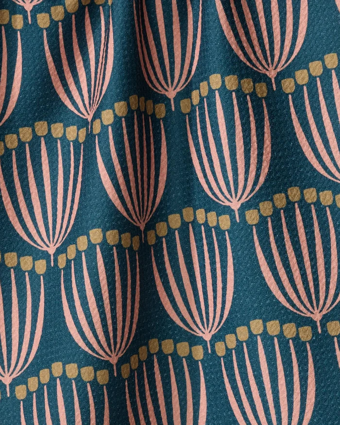 A close-up of the Josie tea towel by Amy MacCready shows its eco-friendly, textured fabric with stylized pink flowers and yellow dots on dark teal. Gentle folds in the towel add to its cozy, inviting look.