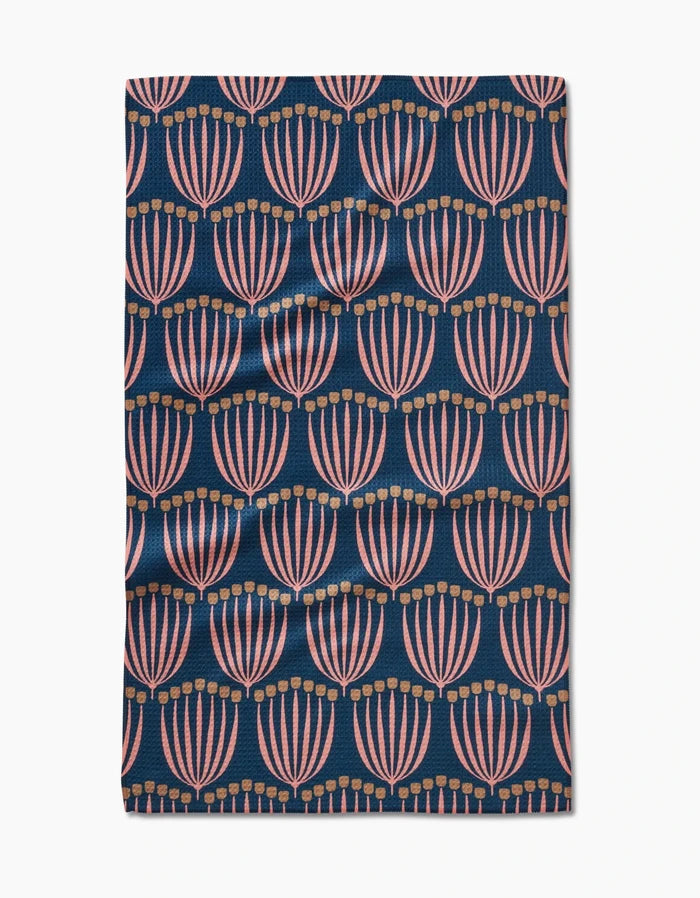 The Josie Geoweave™ tea towel by Amy MacCready features pink and gold stylized floral shapes on a dark blue background. Ultra-absorbent and beautifully designed, its the perfect modern kitchen accessory.