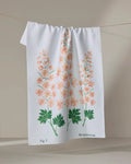 A white tea towel by Linda Fox, called "July Delphinium," hangs on a string and features pink delphinium flowers with green leaves, plus labeled text reading Fig 7 and Delphinium at the bottom.