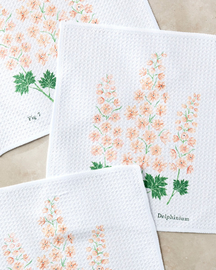 Three white, textured July Delphinium cloths by Linda Fox—made from recycled material—feature embroidered pastel pink delphinium flowers, green leaves, and labels “Delphinium” and “Fig 7,” displayed on a light background.