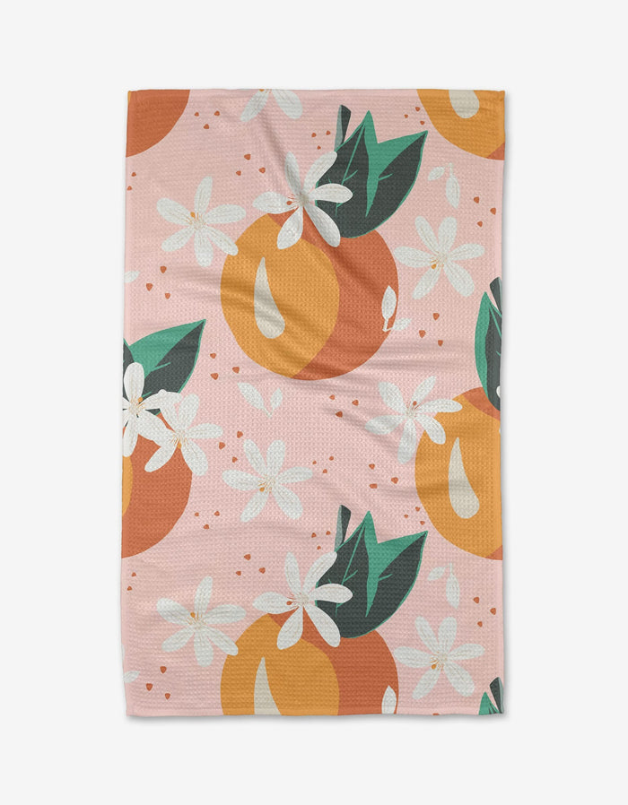 The Just Peachy tea towel by Julianne Haness is pink with a peach pattern, green leaves, and white flowers, made from recycled materials.