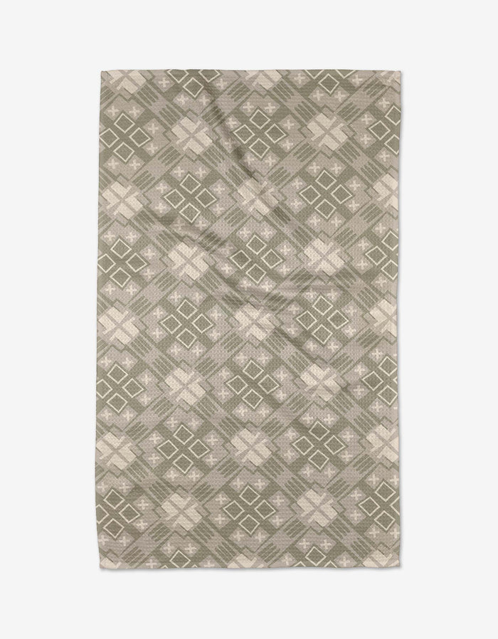 The Ash Cascade Kaleidoscope rug features a symmetrical geometric design with green and beige diamond and cross shapes, crafted from ultra-absorbent Geoweave™ fabric for kitchen tea towel-like durability.