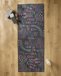 The Jessica Swift "Kind Hearts" yoga mat, red and white with the words kind hearts, kind words, kind thoughts, and kind deeds, rests on a wooden floor with gray yoga blocks, a white water bottle, and a non-slip towel beside it.