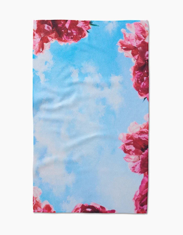 The La Floraison Tea Towel by Stefanie Bales features a blue sky with white clouds and pink flower clusters along the edges, crafted from Geoweave™ fabric for a stylish, functional touch.