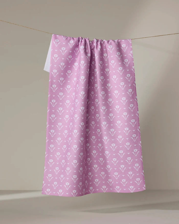 The Ladylake - Pink kitchen tea towel by The Buy Guide, made from recycled materials and featuring a white floral pattern, hangs on a string against a neutral background.