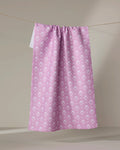 The Ladylake - Pink kitchen tea towel by The Buy Guide, made from recycled materials and featuring a white floral pattern, hangs on a string against a neutral background.
