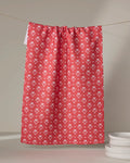 A Ladylake - Red kitchen tea towel by The Buy Guide, featuring a white floral pattern, hangs on a string. Nearby, a small stack of white plates rests on a light surface.