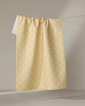 The Buy Guide’s Ladylake - Yellow tea towel, featuring a white floral print on recycled material, hangs on a clothesline against a neutral backdrop. One corner is turned up to show the white reverse side.