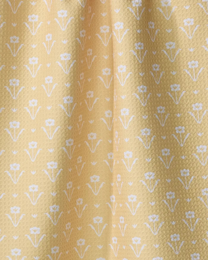 Close-up of Ladylake - Yellow by The Buy Guide: yellow fabric with a subtle textured surface, made from recycled materials, and adorned with small white flowers in neat rows—ideal for a charming kitchen towel.