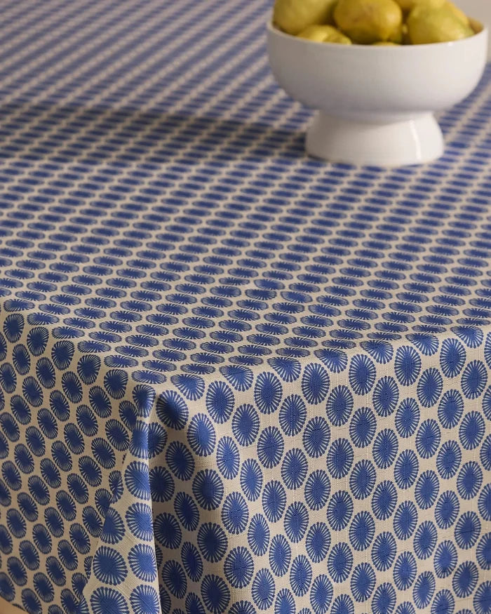 A table is draped with the Geometry Lagoon stain-resistant tablecloth, showcasing blue and white circular patterns, and a white bowl of pears sits near the top right corner.