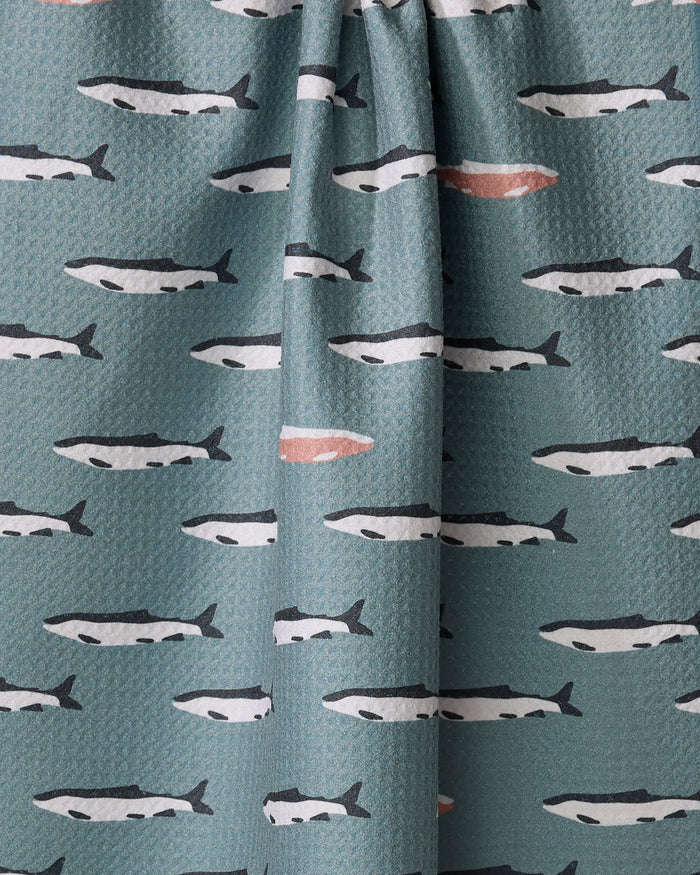 Coit Creative’s “Lake Fish” tea towel features rows of stylized black and white fish swimming on teal, with one standout fish marked in pinkish-orange. Made from recycled materials, it's a sustainable and eye-catching kitchen accessory.
