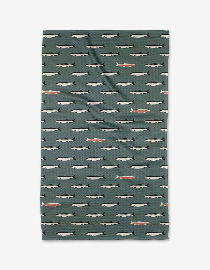 The Lake Fish tea towel by Coit Creative is green, rectangular, and made with Geoweave fabric. It displays rows of illustrated fish in white and gray, with a few orange fish scattered throughout.