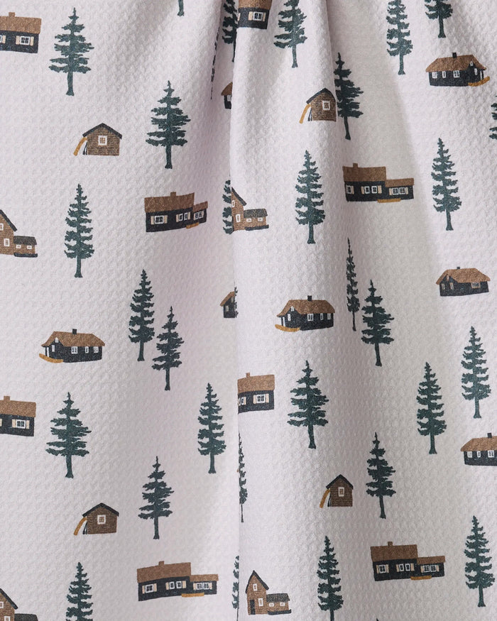 The Lakehouse Cabins kitchen towel by Coit Creative features white textured fabric with green pine trees and brown cabins, offering an ultra-absorbent and stylish addition to your kitchen.