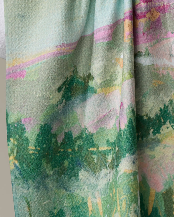 A close-up of Taryn Brennan’s "Land of Milk and Honey" recycled kitchen towel, showcasing its textured fabric and abstract, watercolor-inspired design in green, pink, yellow, and blue reminiscent of a scenic landscape.
