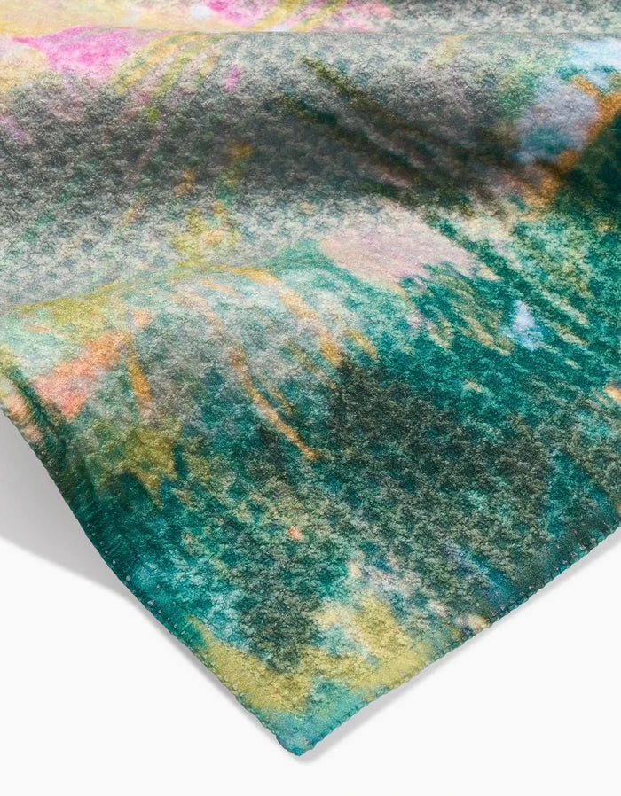 A close-up of the Land of Milk and Honey fabric by Taryn Brennan shows a colorful abstract pattern in green, yellow, pink, and blue on soft Geoweave material with a fuzzy texture and stitched edge.