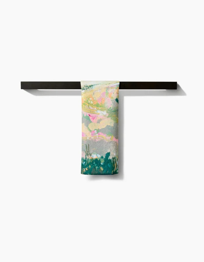 The Land of Milk and Honey Bar Towel by Taryn Brennan, featuring an abstract pastel design and made from recycled materials, is draped over a minimalist black bar set against a plain white background.