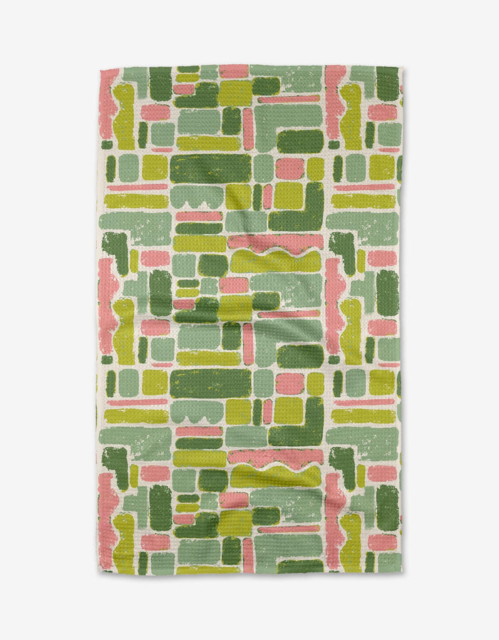 The Kayla Ann Landpatch tea towel features an abstract geometric pattern in green, pink, and mustard yellow on a light background. Made from durable Geoweave fabric, it offers superior absorbency and showcases a stylish overlapping grid design.