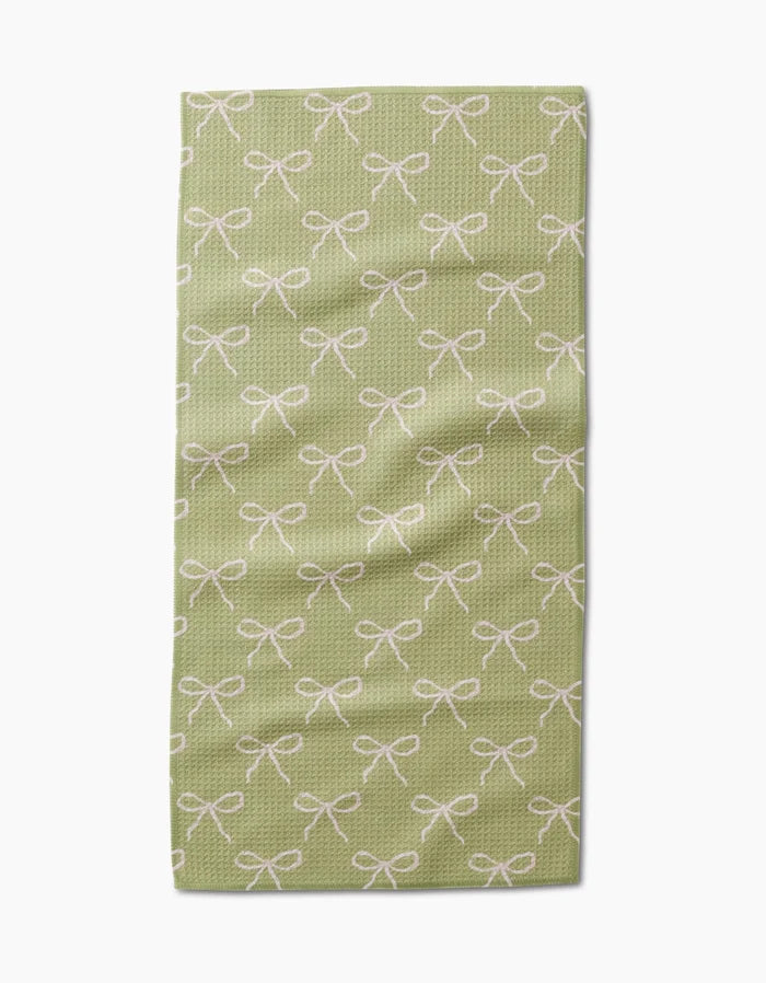 The Laura Prietto Lattice Bows bar towel is light green, made with ultra-absorbent textured Geoweave fabric, and features a repeating pattern of white bows.
