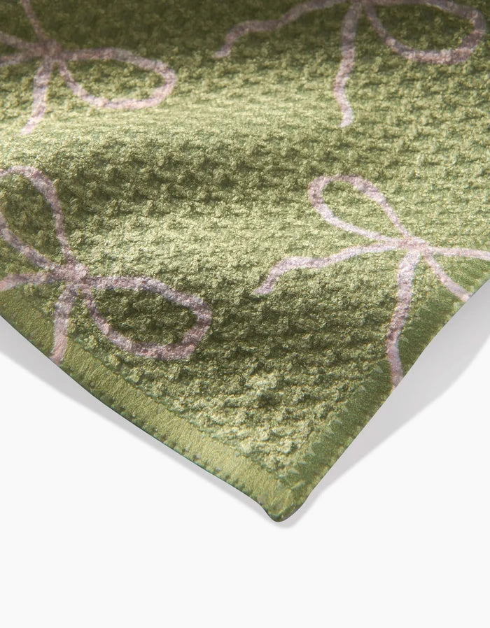 A close-up of the Lattice Bows rug by Laura Prietto shows its green geoweave surface, soft and plush, featuring a textured pattern of light pink line-drawn bows.