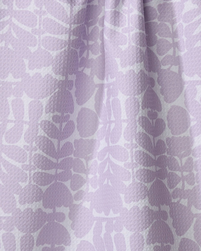 A close-up of the Katie O'Shea "Lavender Scandi Flowers" tea towel, made from recycled materials, with a raised texture and subtle leaf and floral patterns in light and darker purple shades.