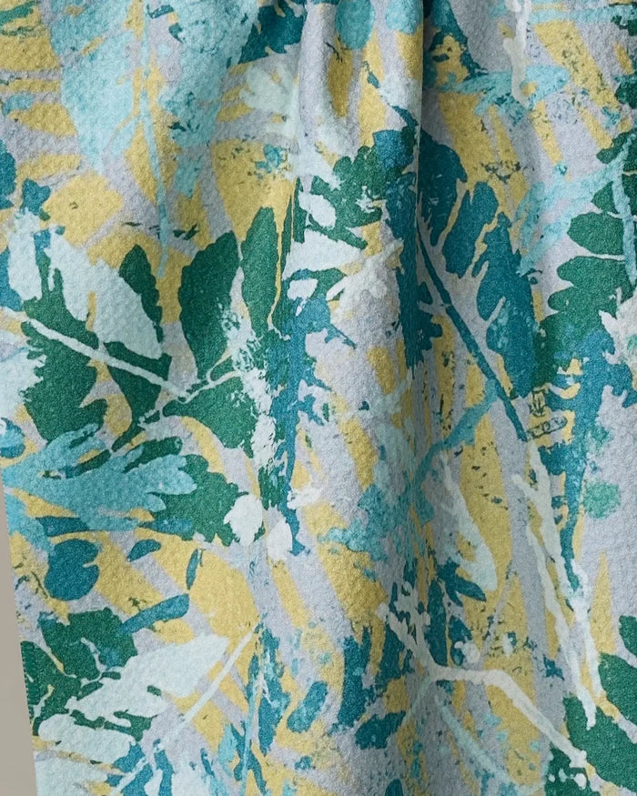 A close-up of the Taryn Brennan Leafy Bush tea towel, showcasing an ultra-absorbent design with overlapping green, blue, and yellow leafy patterns on a light background for an abstract, nature-inspired look.