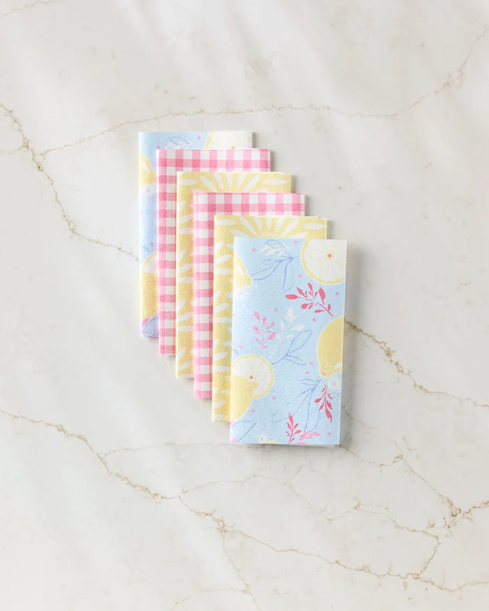 Five folded Ashley Celena "Lemon Pop" eco-friendly kitchen towels are stacked neatly on a marble surface, displaying pastel patterns such as blue with yellow suns and pink with white checkered designs.