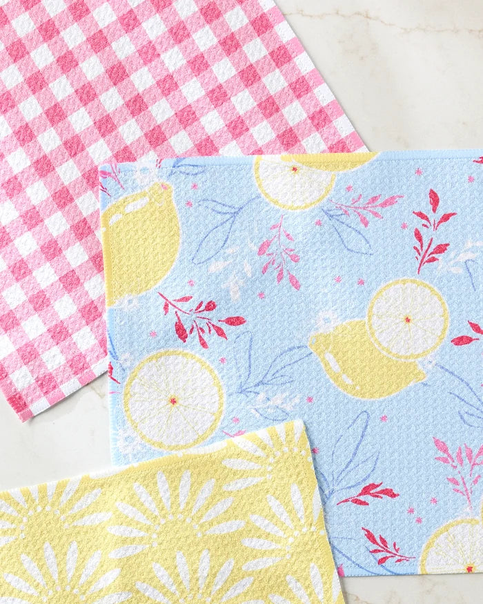 The Lemon Pop dishcloth set by Ashley Celena features three vibrant, recycled designs—red and white gingham, blue with lemons and teapots, and yellow with daisies—to brighten up your kitchen.