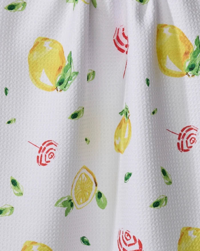 The "Lemons in Capri" kitchen towel by Travel Write Draw by Meagan Morrison is white, textured, made from recycled materials, and features yellow lemons, lemon slices, green leaves, and red-striped candy prints scattered over the surface.