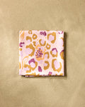The Leopard Loving silk scarf by Elisabeth Wing, made from recycled materials and featuring a pink, yellow, and purple abstract animal print, rests on a textured beige surface.